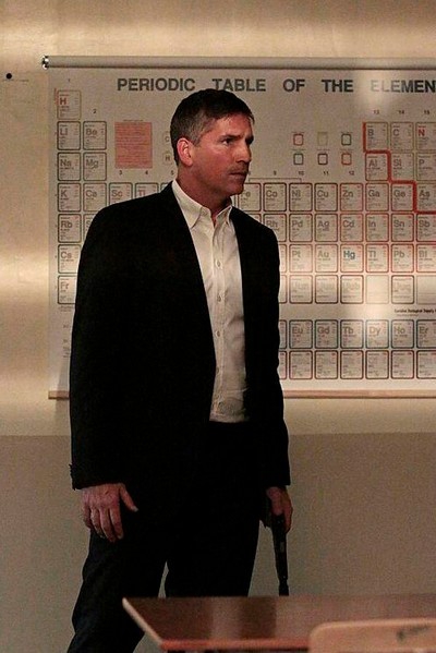 John (Jim Caviezel) devant un tableau périodique des éléments